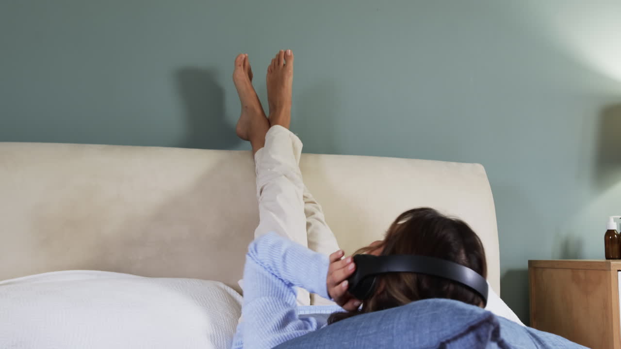 Relaxing at home, woman listening to music with headphones on bed