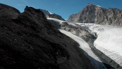 aerial flyover alongside a cliff next to the allalin glacier with allalinhorn peak in view near saas-fee in valais, switzerland on a sunny summer day in the swiss alps