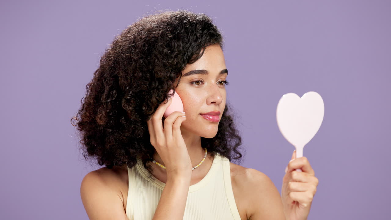 Woman applying makeup using a sponge and mirror