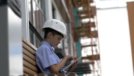 boy builder sits on the bench uses a tablet, monitors the builder project, plays a builder