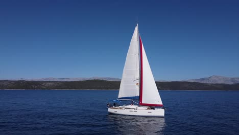 Hermoso-Viaje-En-Velero-Sobre-El-Océano-Con-La-Costa-En-La-Parte-De-Atrás-Mientras-El-Dron-Se-Mueve-Hacia-La-Izquierda-Manteniendo-El-Rumbo-A-La-Vista-De-La-Cámara