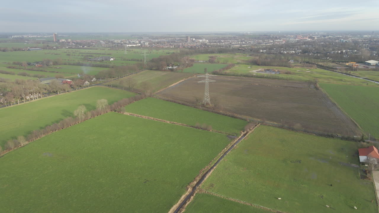 High aerial of large electricity transmission towers in countryside with a city in the background