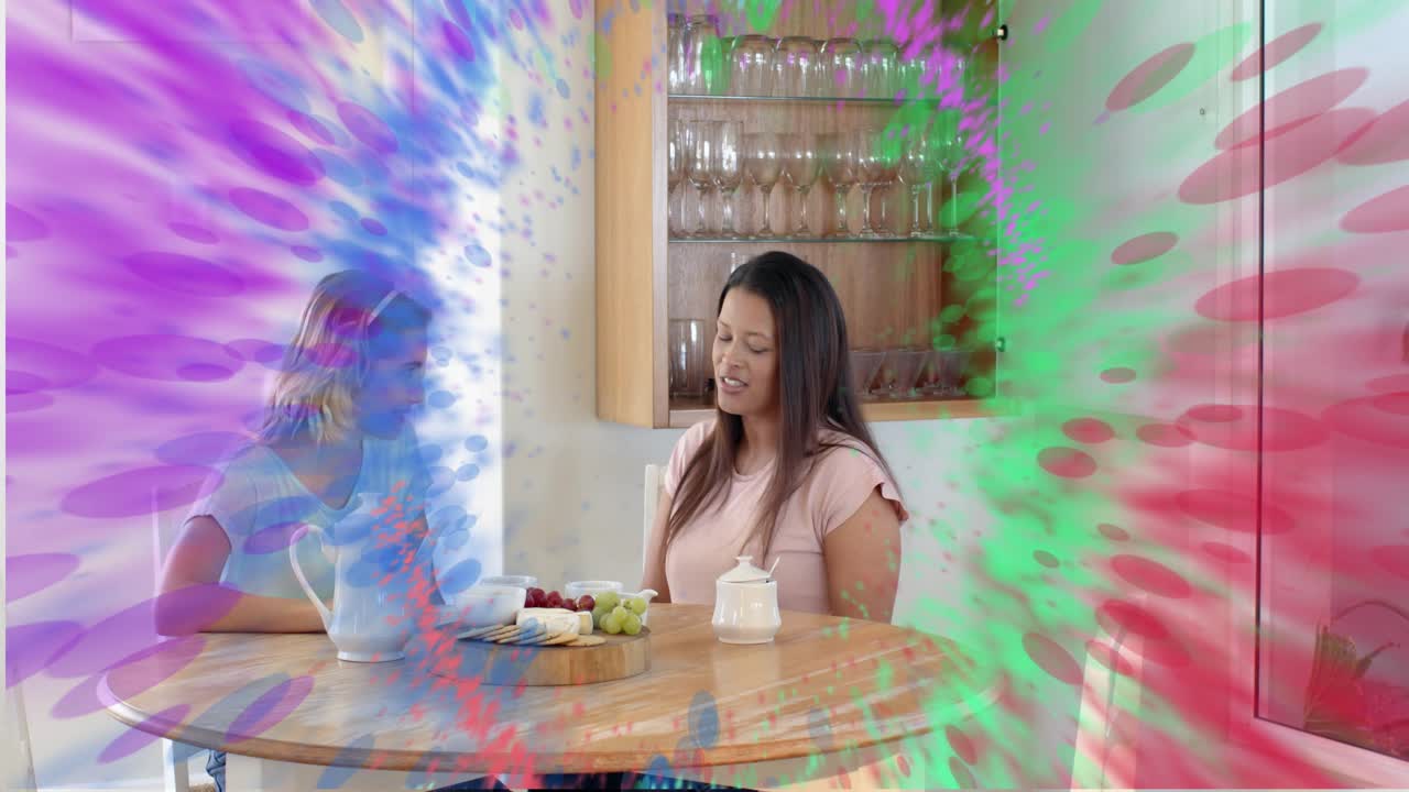 Women at table, left pouring tea, expanding color ring obscuring pour while sharing tea for home