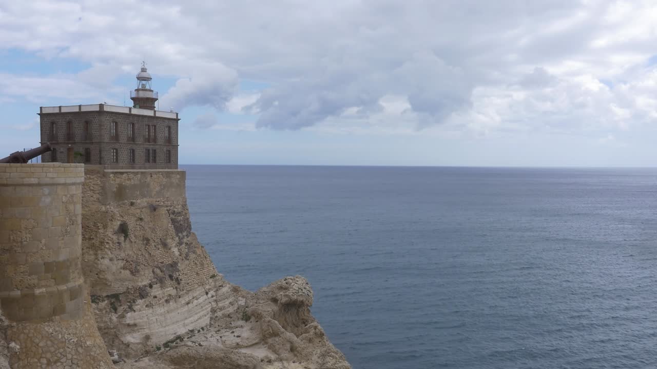 Panoramic view of the Melilla lighthouse, on a rocky cliff, with the Mediterranean Sea in the background and a cloudy sky