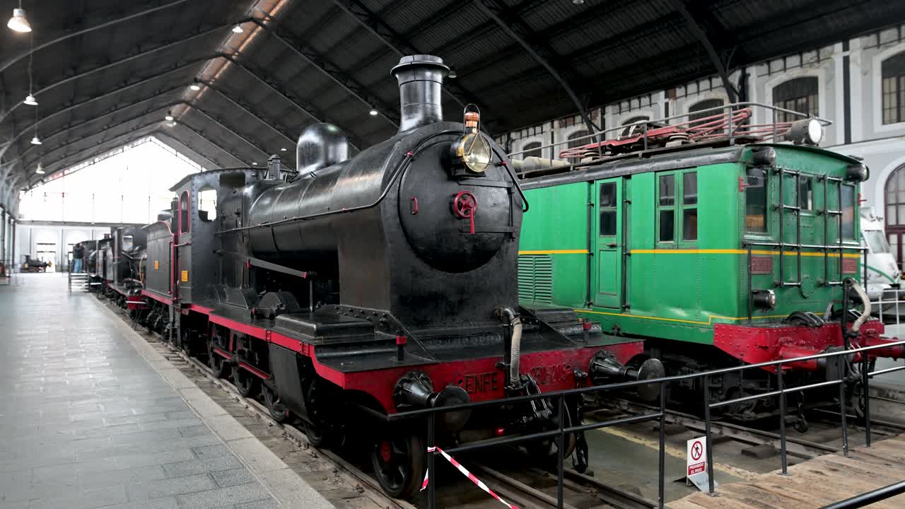 A view inside the historic Madrid Railway Museum (Museo del Ferrocarril), showcasing a collection of preserved locomotives and vintage train cars from Spain's rich railway heritage.