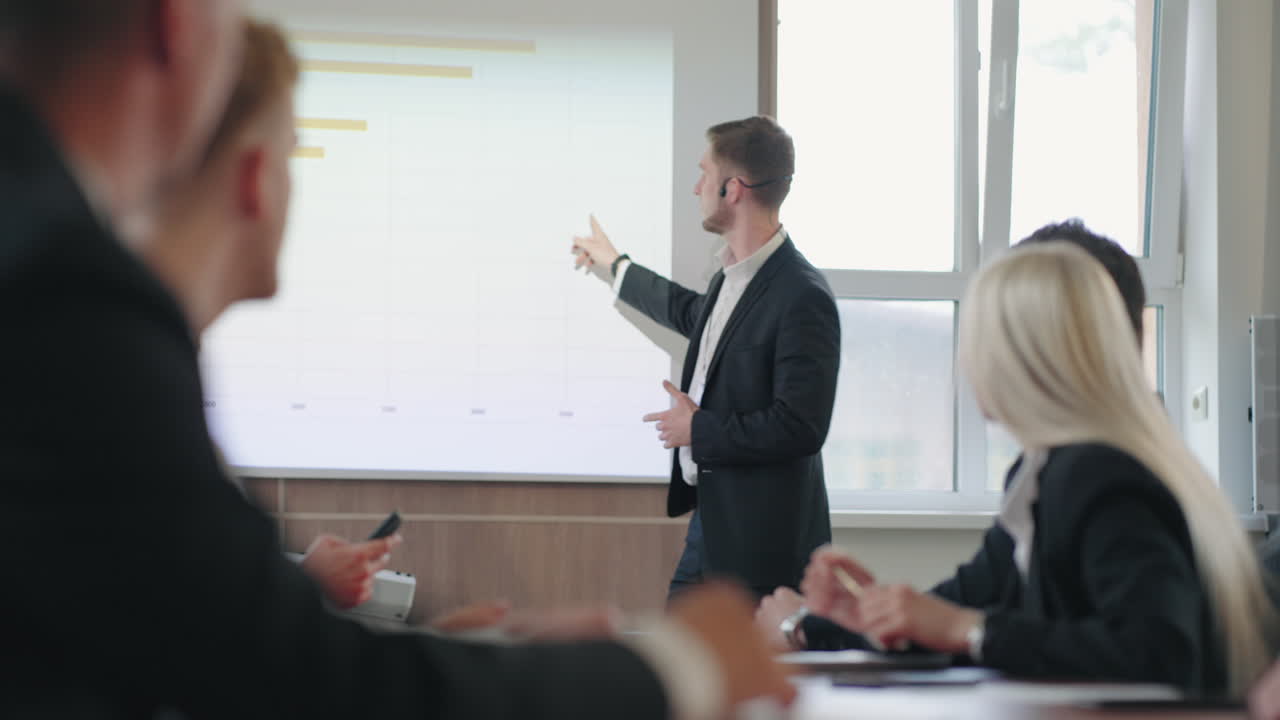 남성 마케팅 전문가가 큰 회사에서 비즈니스 회의에서 이야기하고 있습니다. 남자는 차트를 보여주고 있습니다.