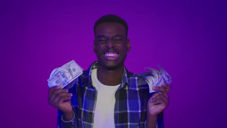 african american guy holding money smelling shaking cash, purple background