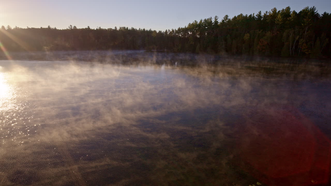 Drone captures tranquil morning mist lifting off water in soft sunrise light