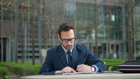 Young-businessman-in-30th-working-with-papers,-writing-notes-in-clipboard,-study-working-materials-lunchtime-outdoors-in-a-park