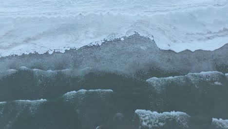 foamy waves lapping at the frozen edge of a serene lake, captured in the dim light of dusk