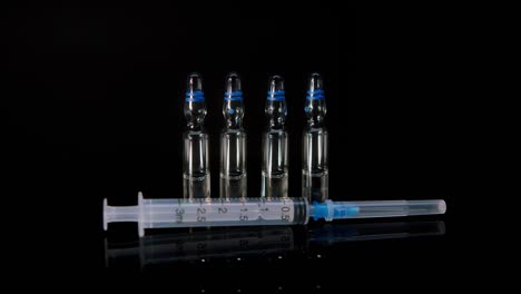 close-up of syringe and ampoules with vaccine against coronavirus. showing sample of medicine on black background, vaccination against covid-19, laboratory research concept