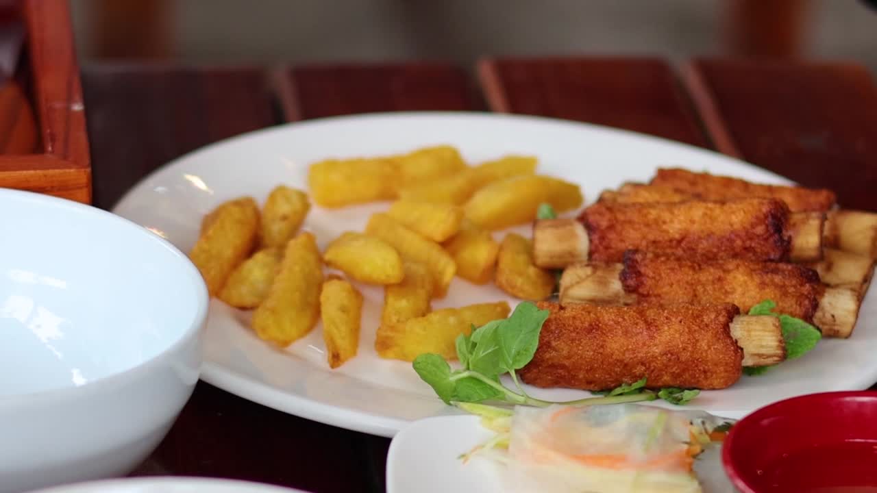 A hand arranges crispy shrimp and golden potatoes on a white plate with fresh greens.