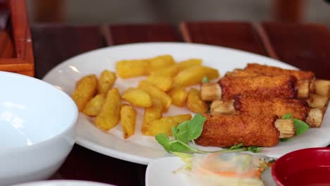 a hand arranges crispy shrimp and golden potatoes on a white plate with fresh greens.