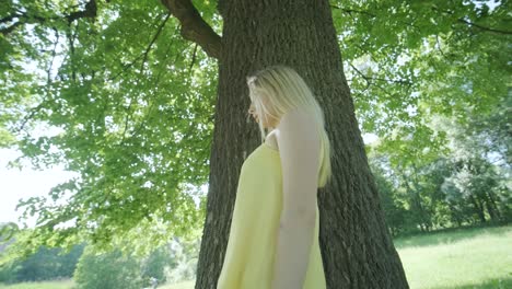 woman in yellow dress dancing by tree in summer park