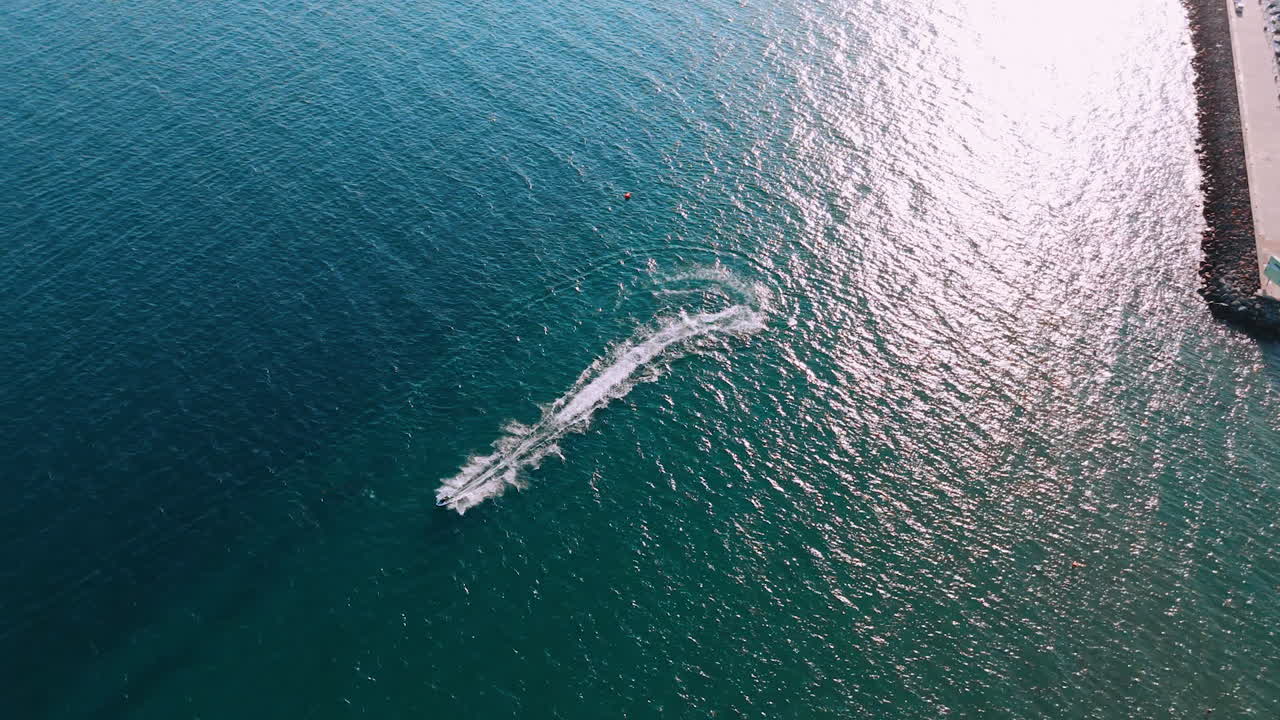 Watercraft maneuvers in coastal waters. A watercraft makes a sharp turn in clear coastal waters, with a marina visible in the sunny background