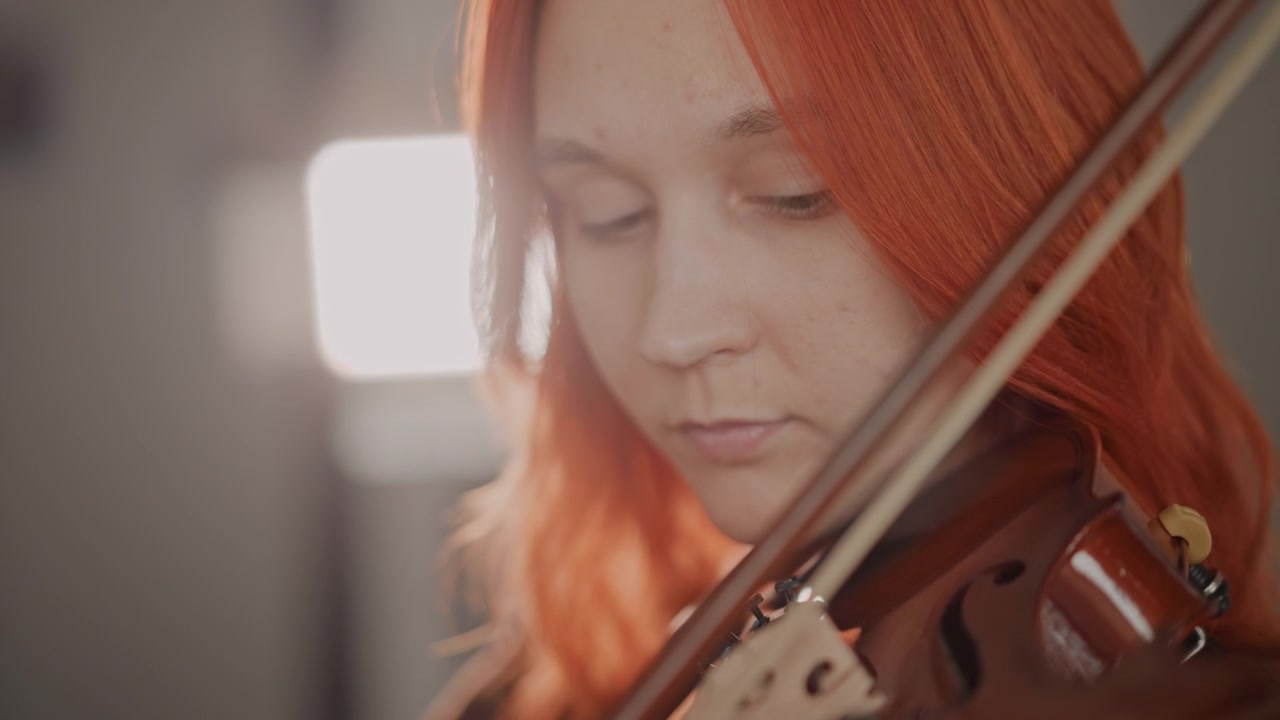 Lidenskapelig fiolinserenade. Uttrykksfull kvinnelig musiker fremfører hjertevarme melodier med myk belysning. Lidenskapelig kvinne med rødt hår fremfører et ømt fiolinstykke under varme lysforhold