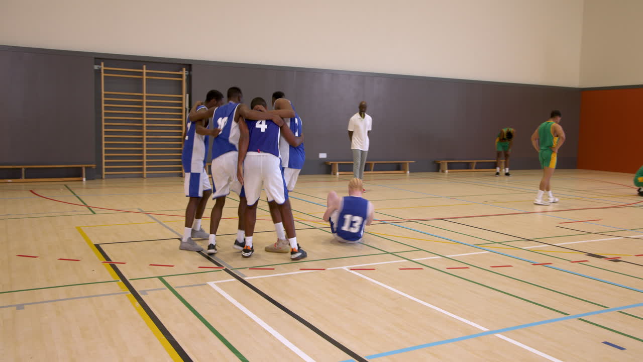 Duas equipes de jogadores de basquete masculinos multirraciais com treinador, uma equipe celebrando a vitória no ginásio.