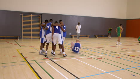 two teams of multiracial male basketball players with coach, one team celebrating victory in gym