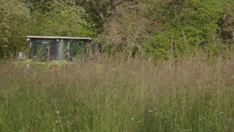 Tractor-harvesting-grass-for-hay-beyond-overgrown-grass