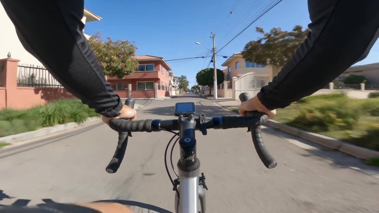 Ciclista segurando o guidão, vestindo uniforme preto, pedalando inclinado em rua suburbana com ciclocomputador