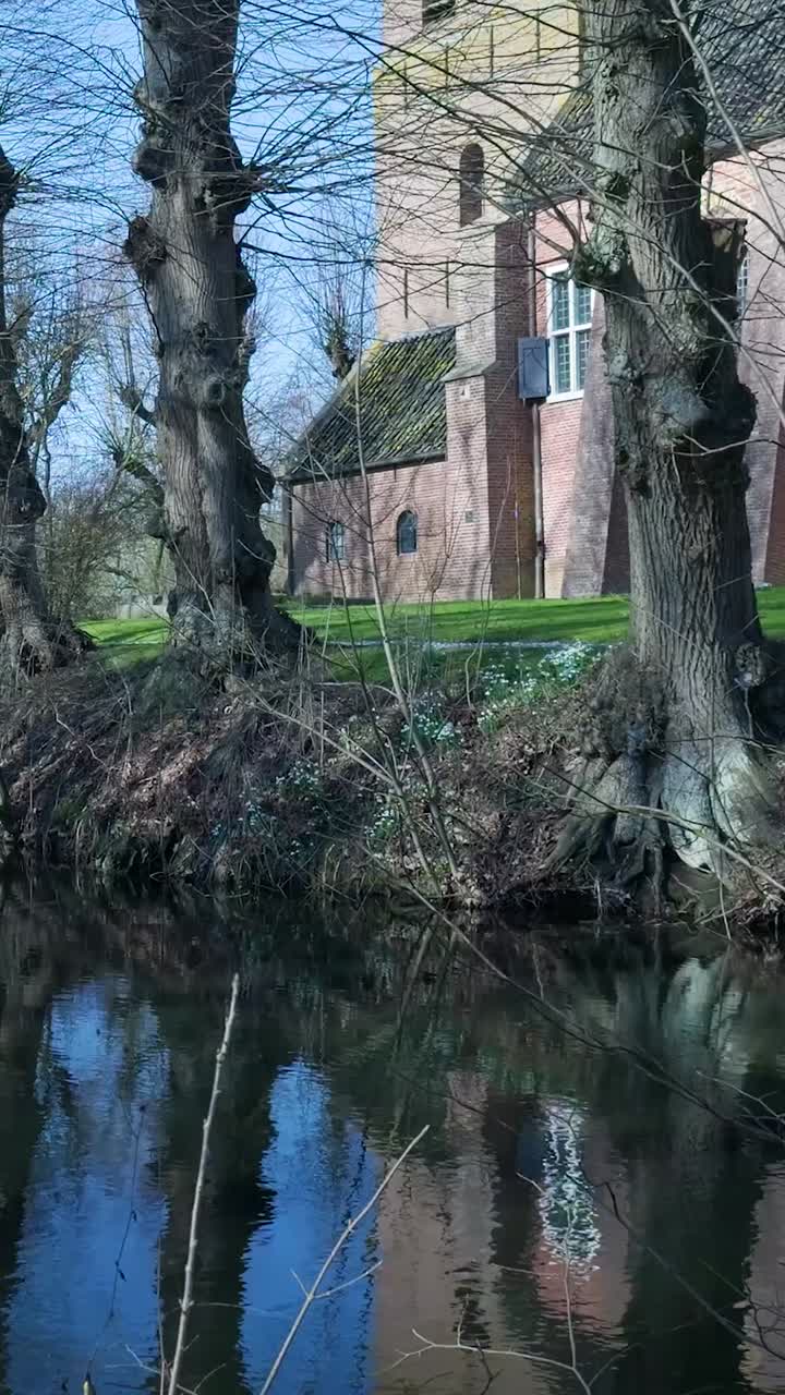 Chiesa storica in mattoni riflessa in acqua calma con alberi spogli