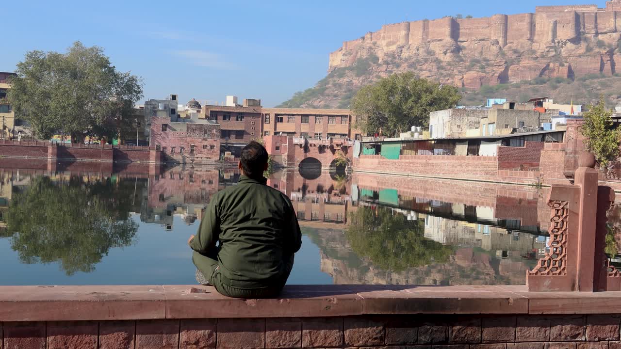 joven meditando en la costa del lago prístino con el reflejo del agua y el cielo azul por la mañana el video fue tomado en gulab sagar talab jodhpur rajasthan india