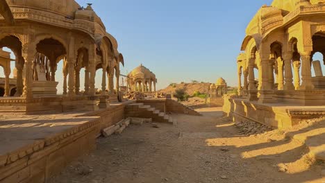 bada bagh in jaisalmer, rajasthan, is a beautiful desert site with clear sky and stunning architecture. the sun shines brightly on this historic garden, featuring royal cenotaphs
