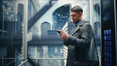 successful businessman riding glass elevator to office in modern business center. handsome happy man smile while using smartphone, write text message, check social media and work emails in a lift.