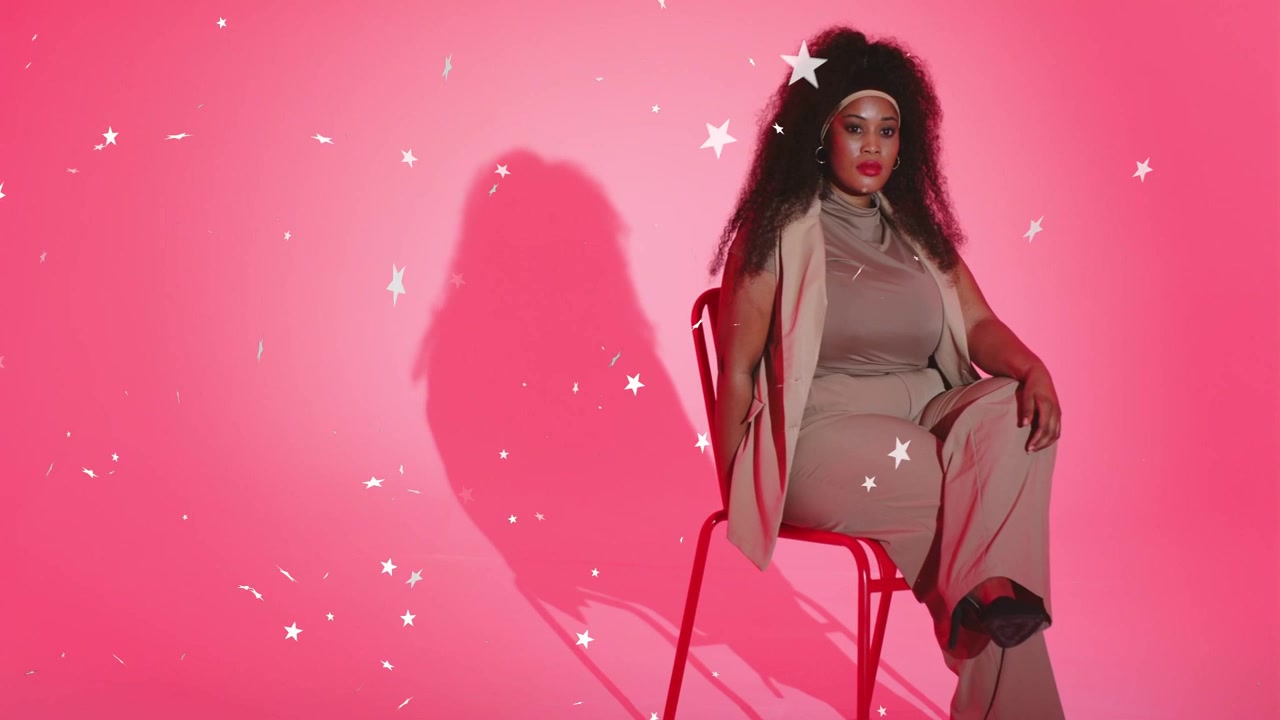 Mujer sentada en silla roja en estudio rosa, estrellas animadas flotando hacia la izquierda y realzando el look de moda