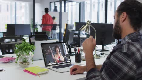 hombre de negocios de raza mixta sentado en un escritorio usando una computadora portátil haciendo una videollamada con una colega