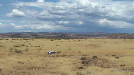 Vista-Aérea-Rastreando-Un-Vehículo-Eléctrico-Conduciendo-En-Medio-De-La-Sabana-Soleada