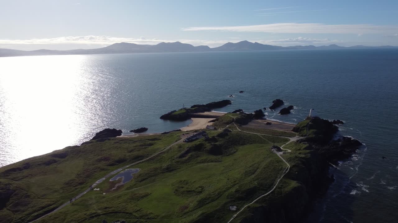 yynys llanddwyn 웨일스 섬을 내려다보는 공중 뷰. 해가 뜨는 스카이라인을 가로질러 반 ⁇ 이는 바다와 안개가 있는 스노우도니아 산맥