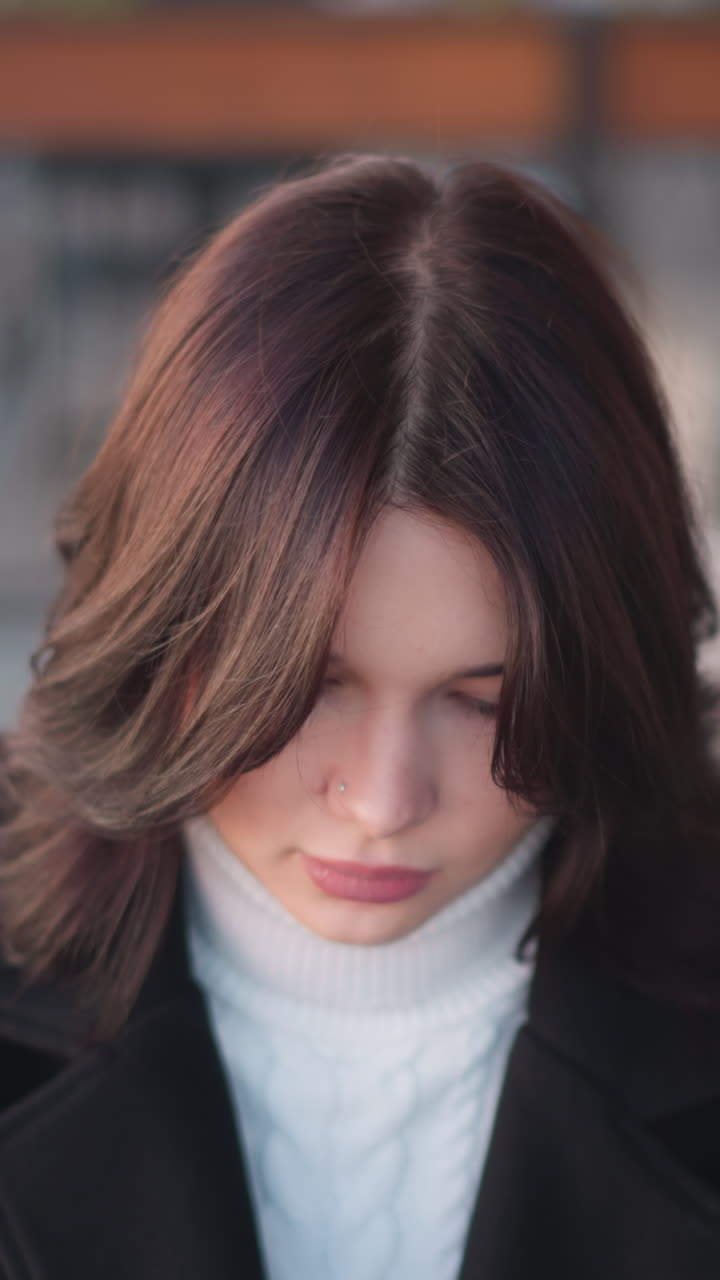 dama sentada con expresión enfocada, algo delante de ella, el viento balanceando suavemente su cabello en un entorno al aire libre, iluminación suave, fondo borroso