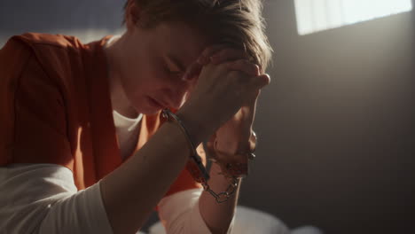 female inmate in handcuffs whispering prayer in prison cell