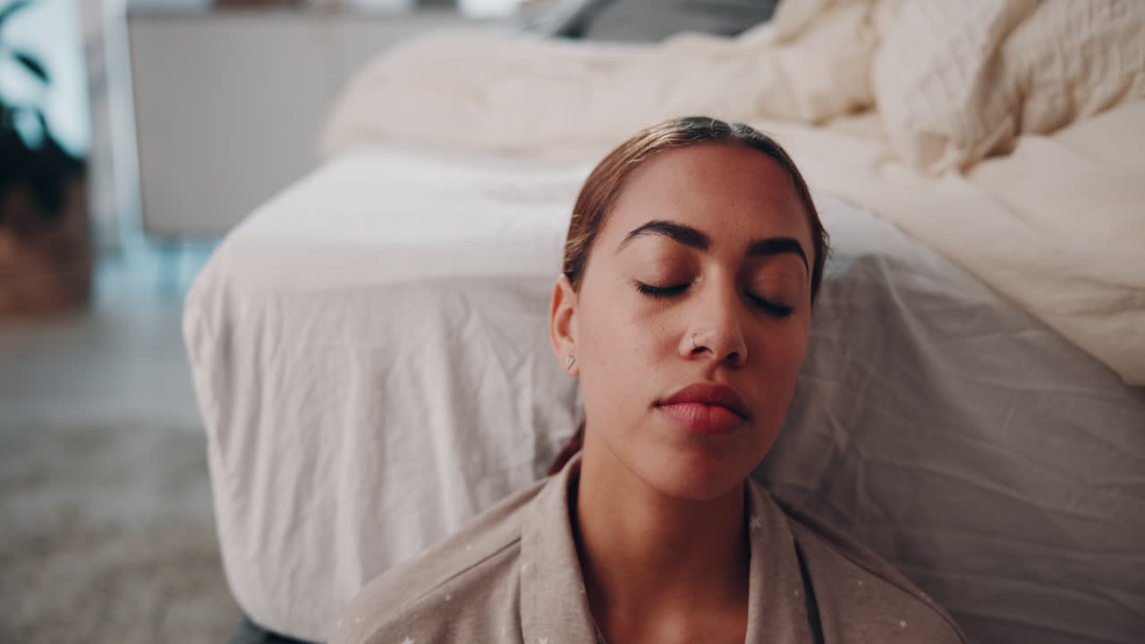 mujer sentada en el suelo de un dormitorio, con los ojos cerrados y relajada