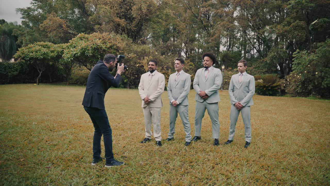Un fotografo riprende i testimoni dello sposo durante un servizio fotografico di matrimonio all'aperto.