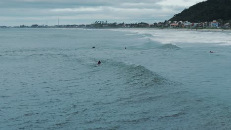 Surfers-Floating-in-Water-as-Waves-Carry-them-Away,-City-in-Background