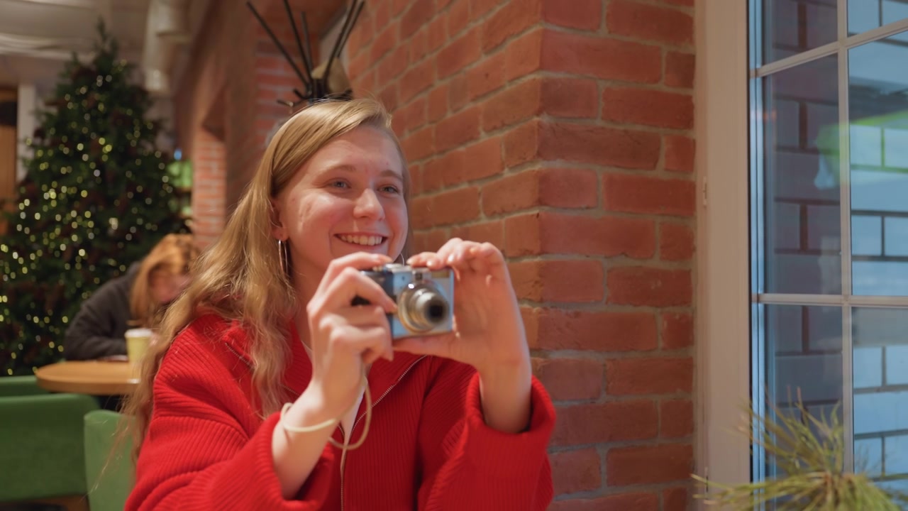 Smiling Young Woman Takes Photo with Digital Camera in Cafe