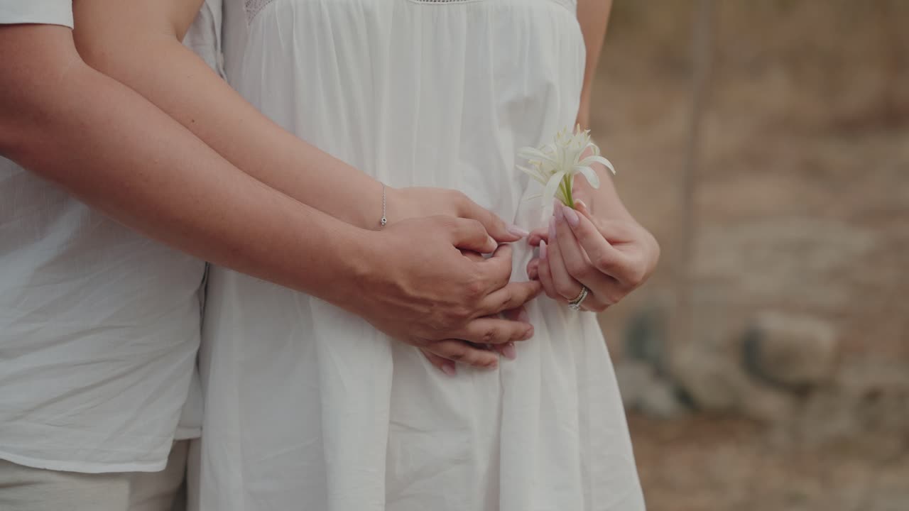 하얀 꽃을 들고 애틋하게 껴안은 흰색 의상을 입은 커플의 클로즈업