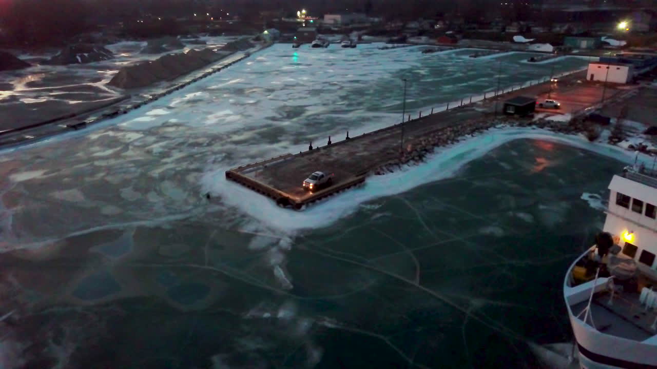 해질 무렵 캐나다 겨울 동안 얼어붙은 호수로 둘러싸인 부두 끝에 앉아 있는 픽업 트럭 주위를 왼쪽으로 돌고 있습니다.