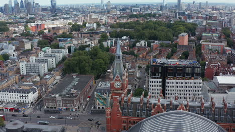 Descending-footage-of-old-brick-building-with-clock-tower.-Tilt-up-reveal-cityscape-with-skyscrapers-in-distance.-London,-UK