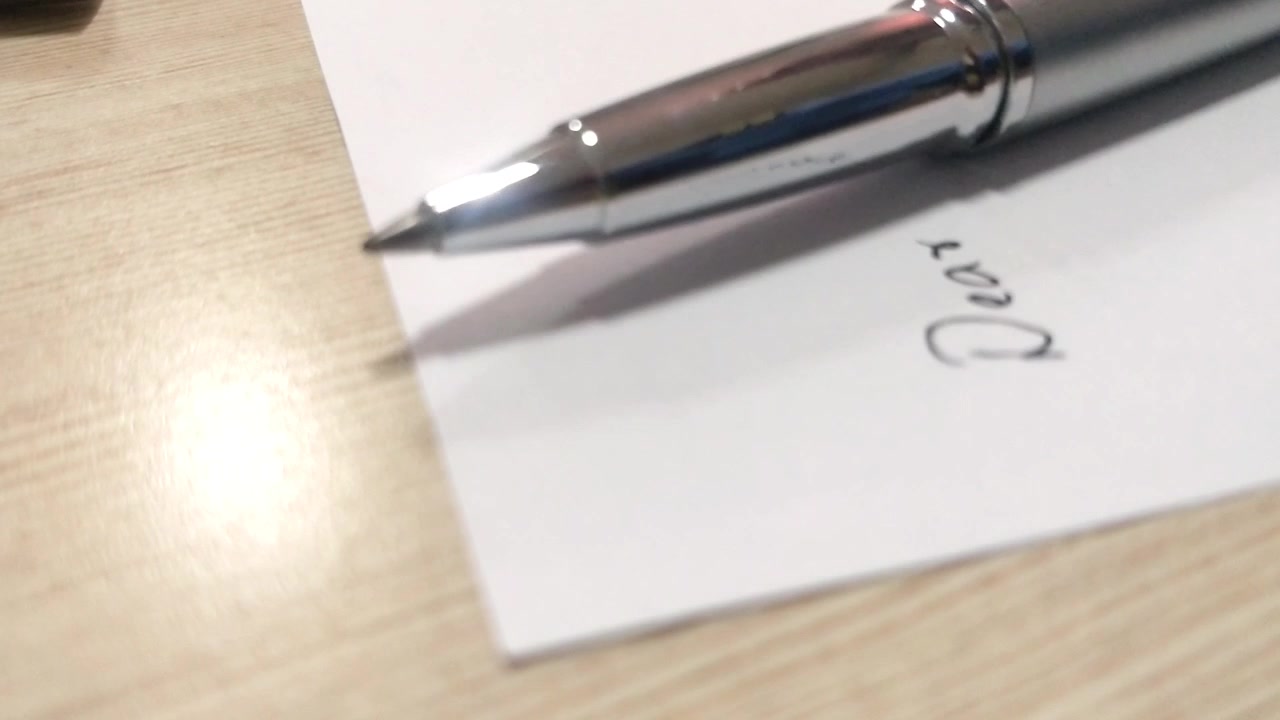 Penbevægelse i sidelæns retning. En hånd holder en pen, skriver 'dear' og slipper den ned. Pennen svinger sidelæns