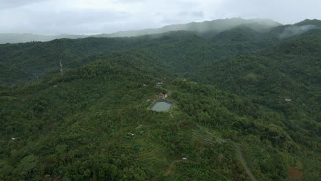 Luftaufnahme-Eines-Wasserspeicherbeckens-Inmitten-Eines-Bergwaldes-Und-Einer-Plantage