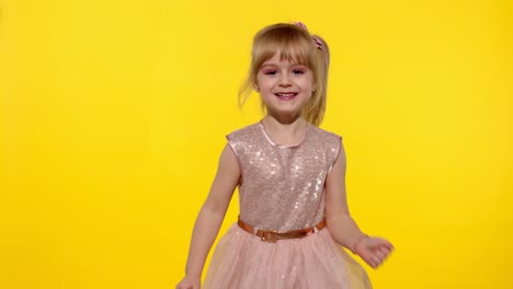 little blonde child girl 5-6 years old smiling, dancing, celebrating on yellow studio background