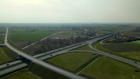 Aerial-shot-of-highway-interchange-surrounded-by-green-fields-and-small-Village-in-background-during-sunny-day