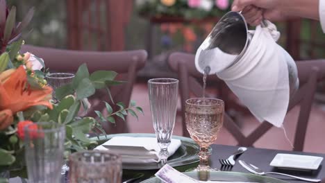 waiter pours water into glass glass during outdoor wedding reception