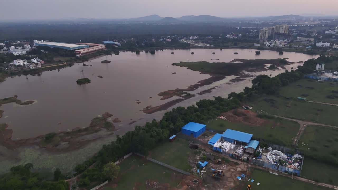 Aerial view of Mambakkam lake located in Chennai near Vandalur. Wide-angle footage of urban expansion at morning. The clip shows a large, placid lake framed by new residential and commercial buildings
