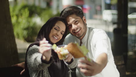 Joven-Pareja-Musulmana-Mostrando-Su-Almuerzo-A-La-Cámara-Y-Comiéndolo.