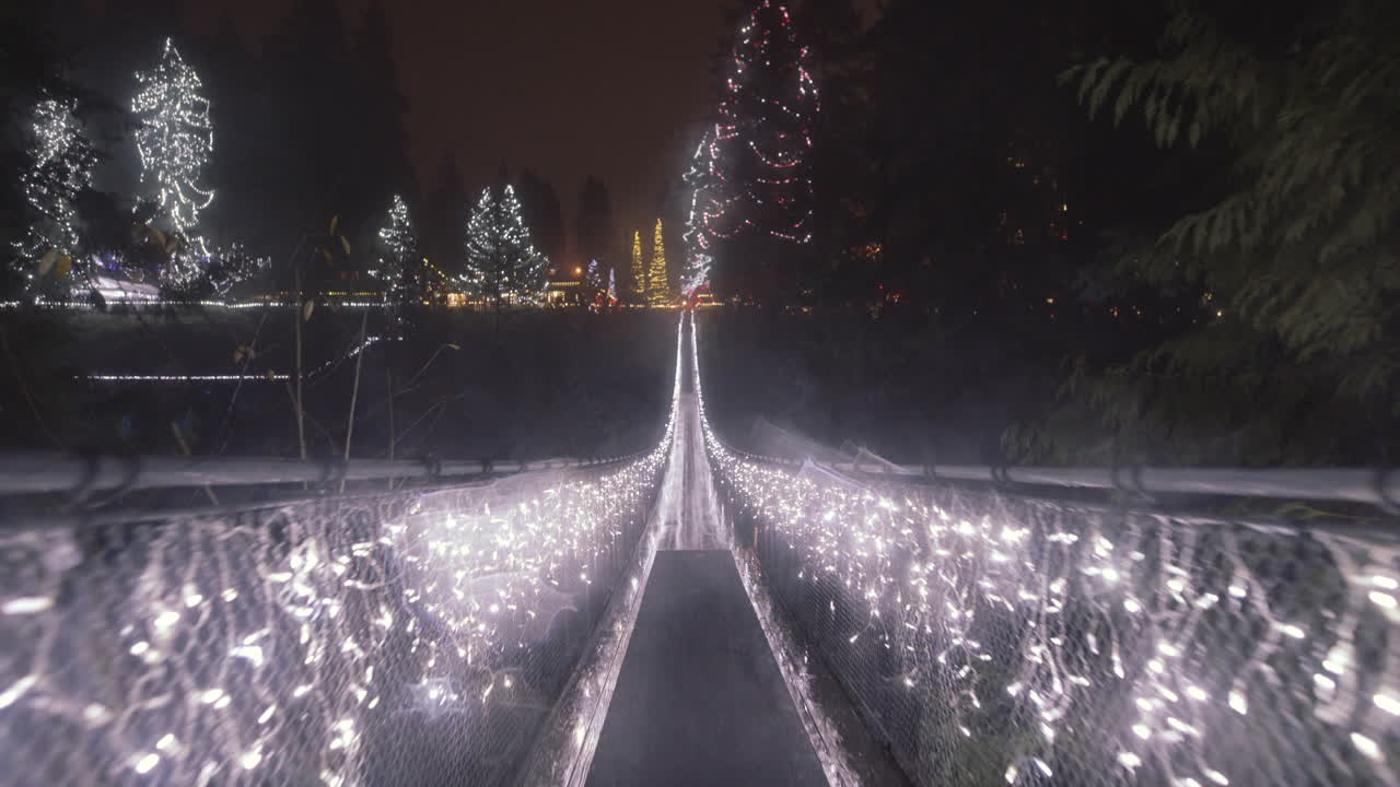 paseo rápido a través de un largo puente colgante decorado con luces navideñas, noche lluviosa