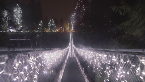 Paseo-Rápido-A-Través-De-Un-Largo-Puente-Colgante-Decorado-Con-Luces-Navideñas,-Noche-Lluviosa